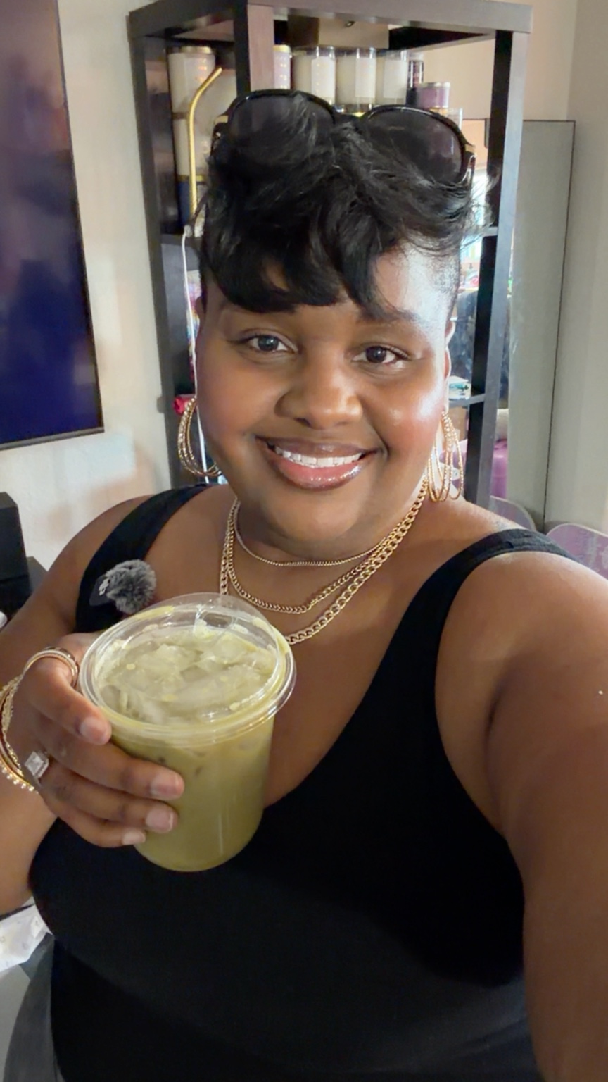 Lea smiling in a black outfit and holding an iced matcha
